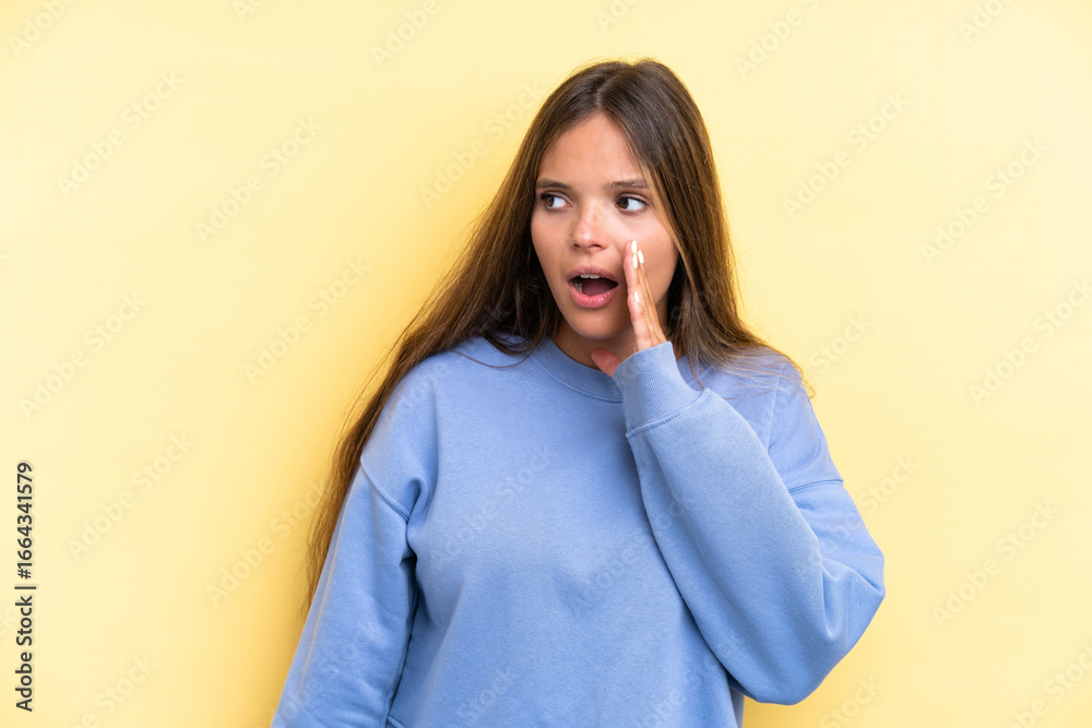 Young caucasian woman isolated on yellow background whispering something with surprise gesture while looking to the side Young caucasian woman isolated on yellow background whispering something with surprise gesture while looking to the side