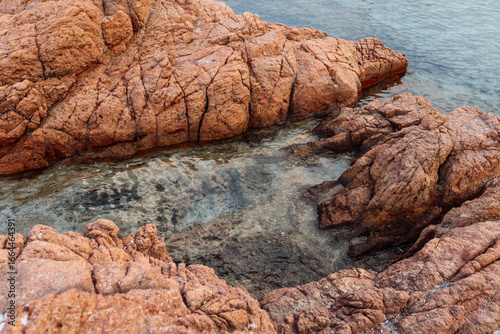 Pink granite coastal rocks and clear turquoise sea water. Natural seascape photography. Coastal landscape and travel destination concept. Design for poster, wallpaper, postcard. Top view.
