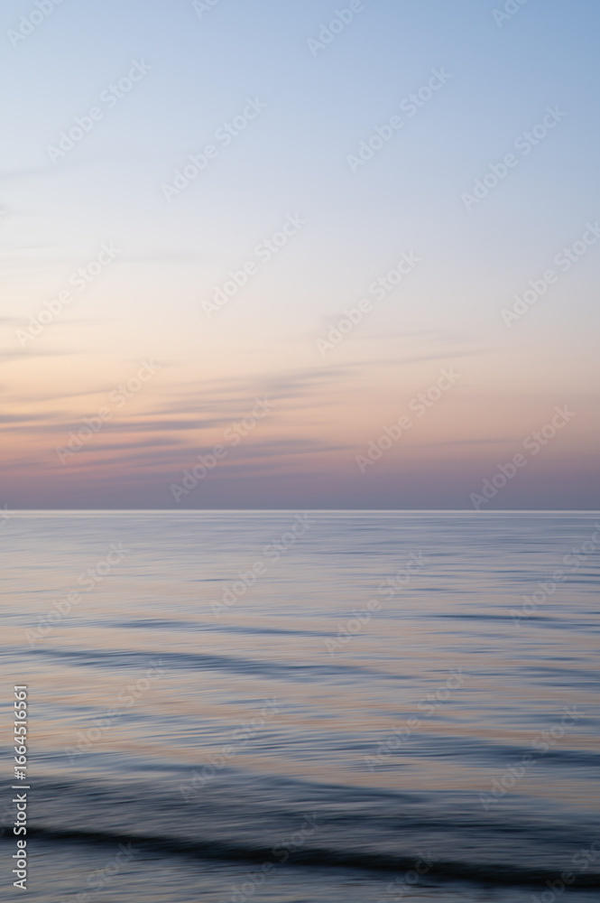 Fototapeta premium A dreamy, impressionistic paint like blurred sea sunset background with gently soft pastel colours. Vertical photo.