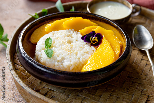 Thai mango sticky rice with coconut milk, garnished with edible flowers and mint on the table close up