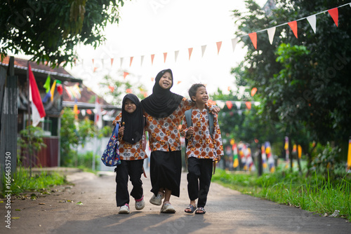 Three indonesia children happily walking together on a village road, wearing matching batik clothes and carrying school bags. Joyful friendship and family moment.