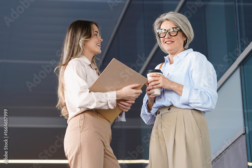 Tapeta Two businesswomen are having a conversation outside their office building, holdi
