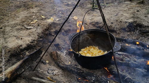 cooking on the fire. Rustic Campfire Cooking in the Wilderness, Traditional Outdoor Meal Over Open Fire, Camping Stew in a Pot Hanging Above Flames, Survival Cooking Scene with Fire and Tripod	
