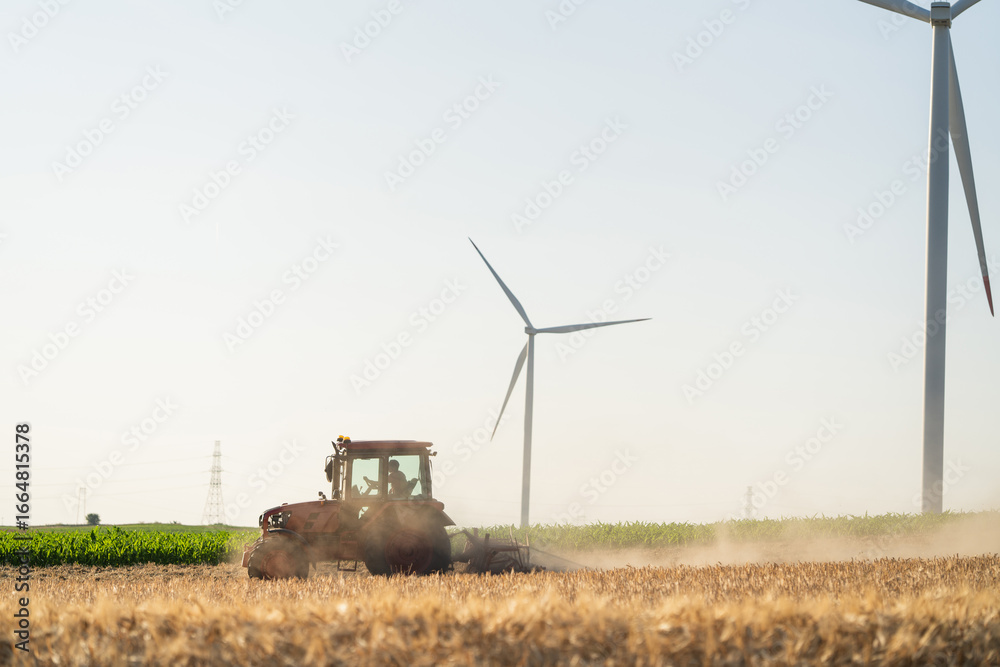 Fototapeta premium Agricultural tractor on the field with wind turbines