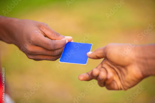 Tablou pe pânză Black african male hands holding exchanging blue card outsde blurred background