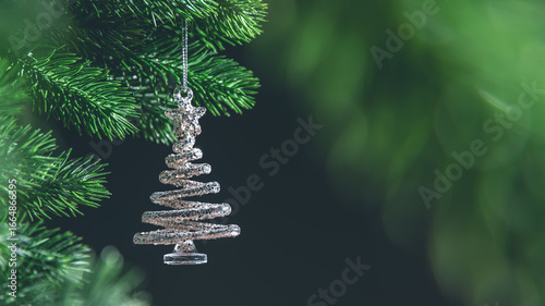 Bild auf Leinwand Silver spiral christmas tree ornament hanging from a green branch on dark backgr