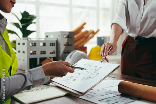 Two architects analyzing blueprints and engaging in a detailed discussion about a building project within the office environment
