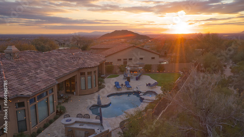 A desert landscaped backyard featuring a travertine tile pool deck, fireplace and outdoor kitchen.