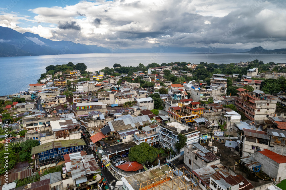 Fototapeta premium Aerial panoramic view of Lake Atitlán and San Pedro in Guatemala with volcanic mountains, lush green landscape, and dramatic sky over Central America
