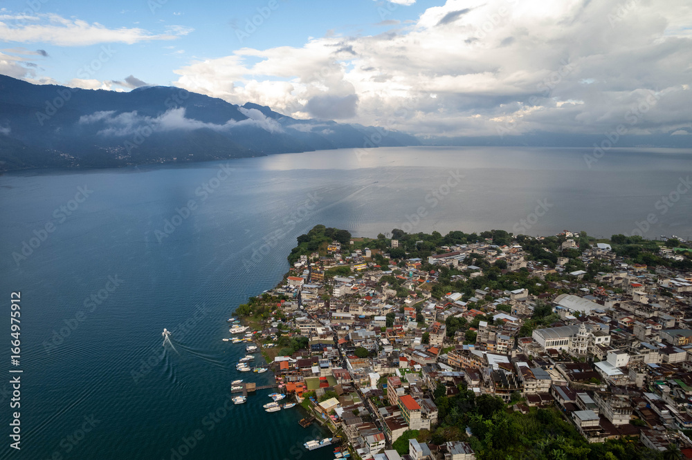 Fototapeta premium Aerial panoramic view of Lake Atitlán and San Pedro in Guatemala with volcanic mountains, lush green landscape, and dramatic sky over Central America