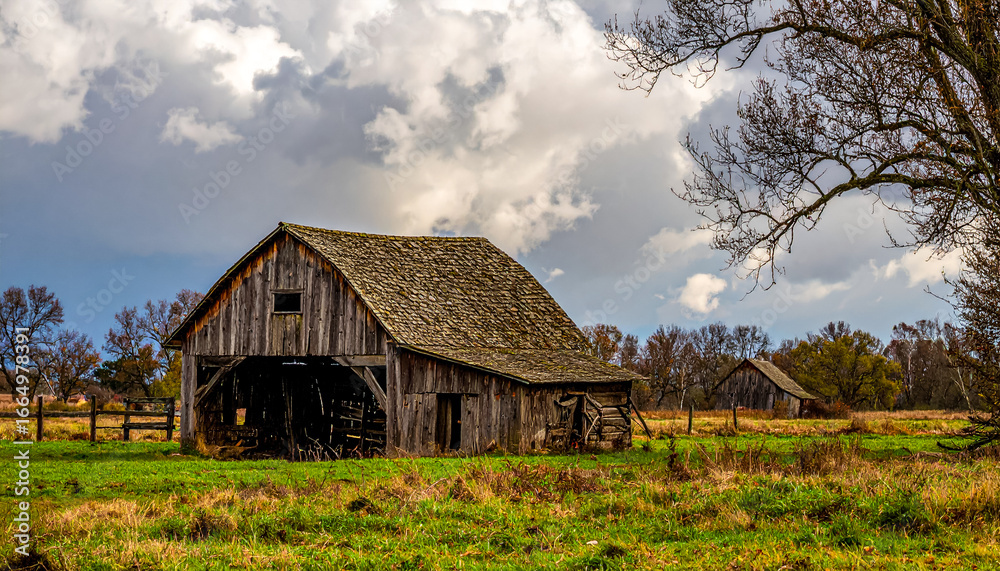 Obraz premium Rustic Wooden Barn in a Grassy Field Under Cloudy Sky