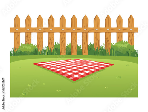 A classic red and white checkered picnic blanket on the grass with a basket and food, in front of a wooden fence