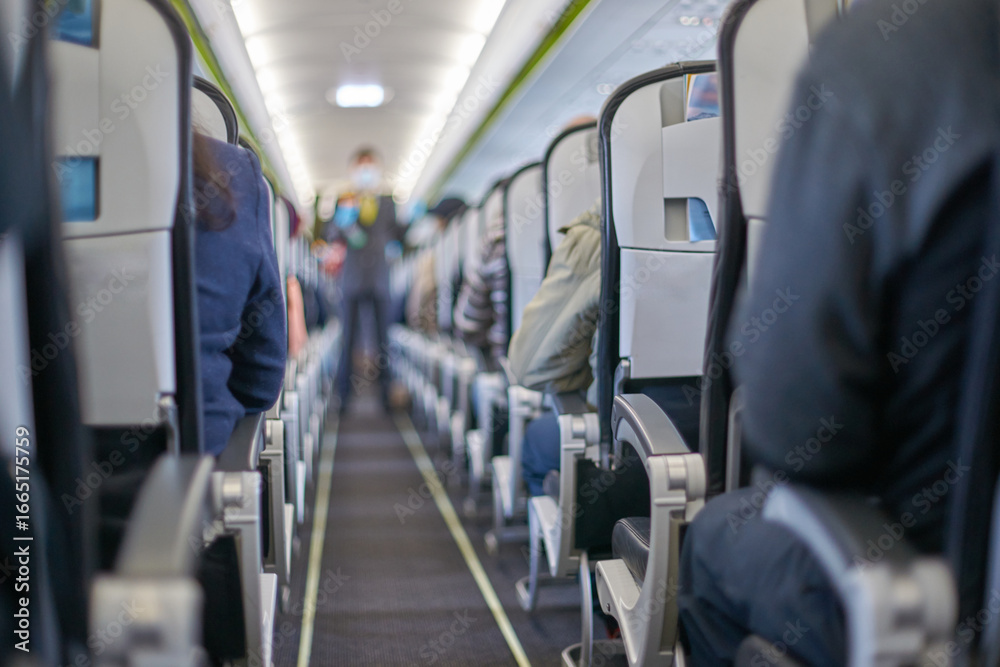 Obraz premium Passengers seated inside airplane cabin during flight journey with focus on aisle and seats.