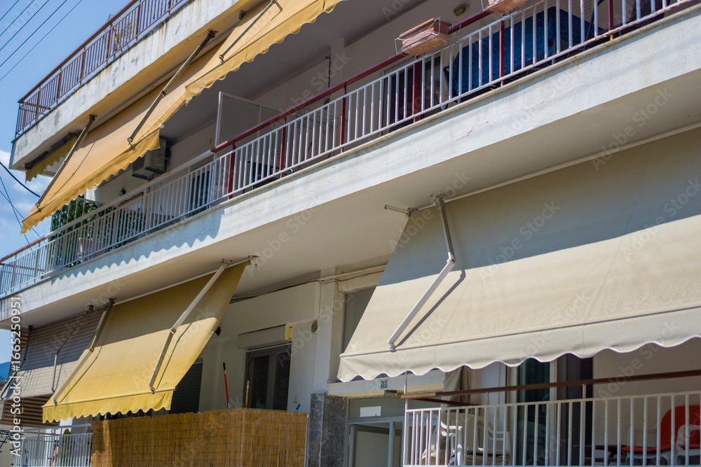 Fototapeta premium residential building facade with retractable awnings extended. a view of a multistory home with balconies and sun shades on a bright, sunny day, of home improvement, sun protection, architecture