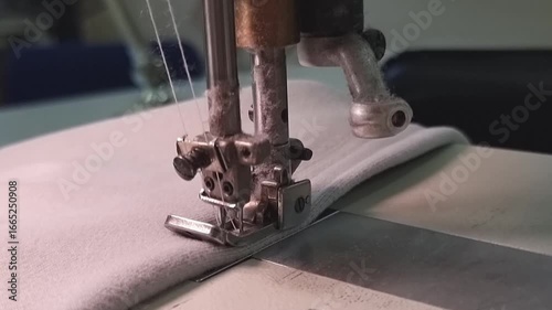A production flat-seam machine makes a close-up stitch on a gray fabric.