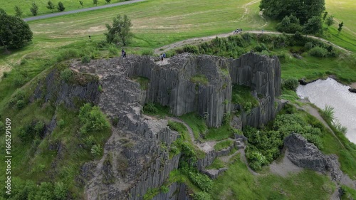 Aerial drone footage of Panská skála in the Czech Republic, a unique volcanic basalt rock formation resembling organ pipes. Scenic view showcasing dramatic geology, natural monument.