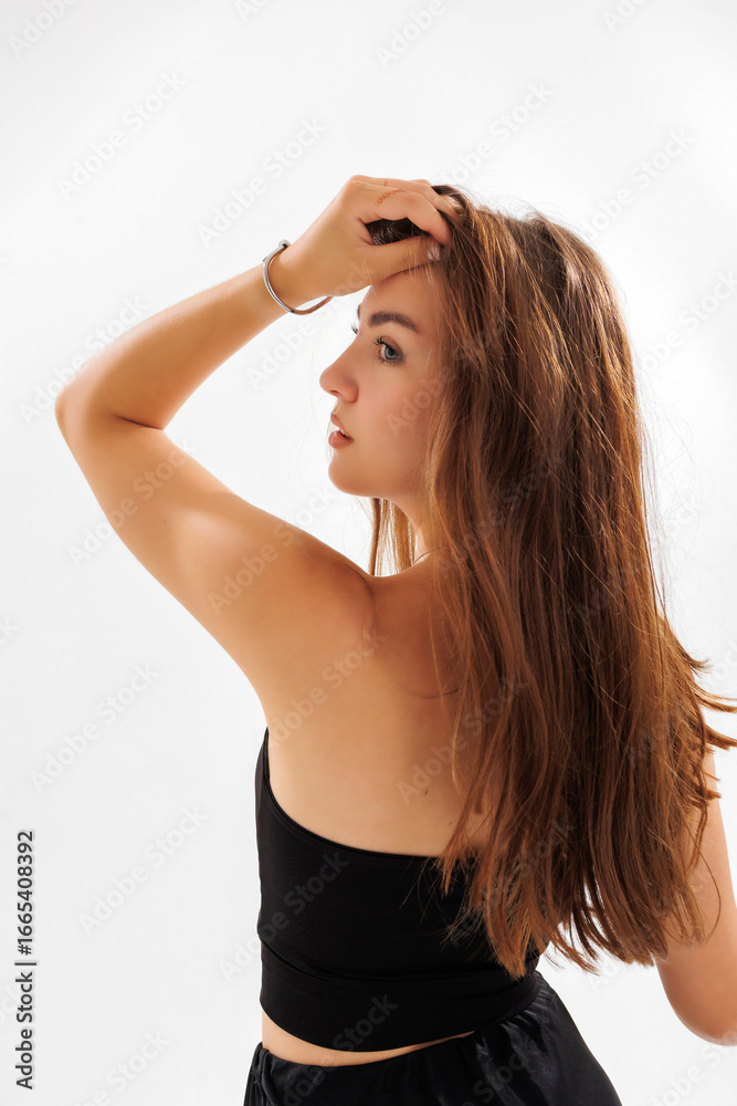 Fototapeta premium Elegant young woman with long hair poses against a white background during a fashion photoshoot in a studio setting