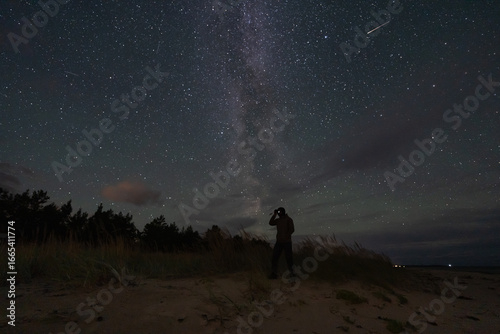 Εκτύπωση καμβά A man's silhouette on a beach using a night vision monocular to explore the magnificent starry sky and Milky Way
