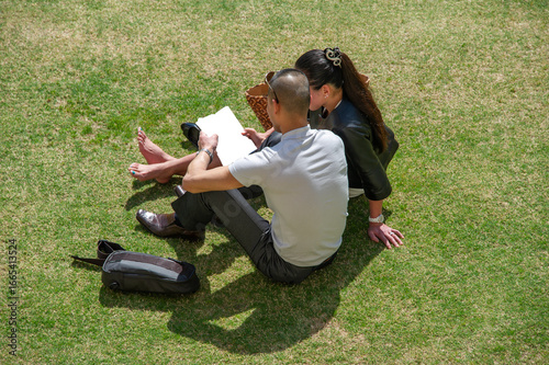 Attractive Anonymous Couple Sit on Grass Reading Magazine (masked)