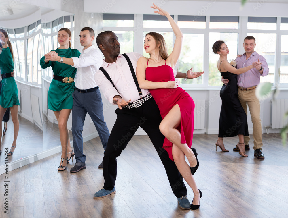 Fototapeta premium With unhurried music, woman with African man in couple spins to rhythm of waltz during lesson for novice students. Classes in mini-groups for those who want to learn dancing