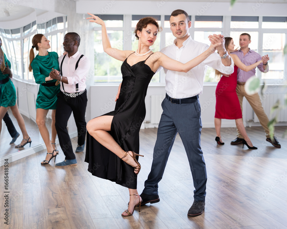 Fototapeta premium Dynamic young male and female attendees of dancing courses doing waltz in group