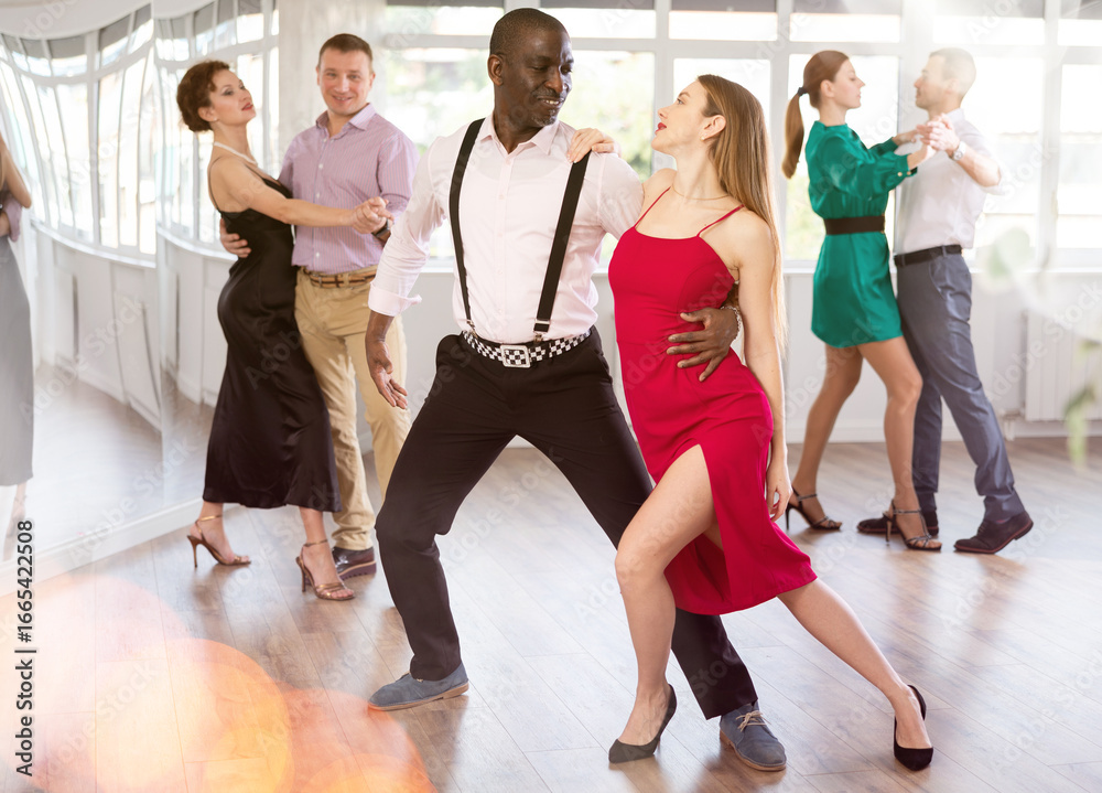 Naklejka premium Gracious man and young woman practicing waltz in pair in dancing studio