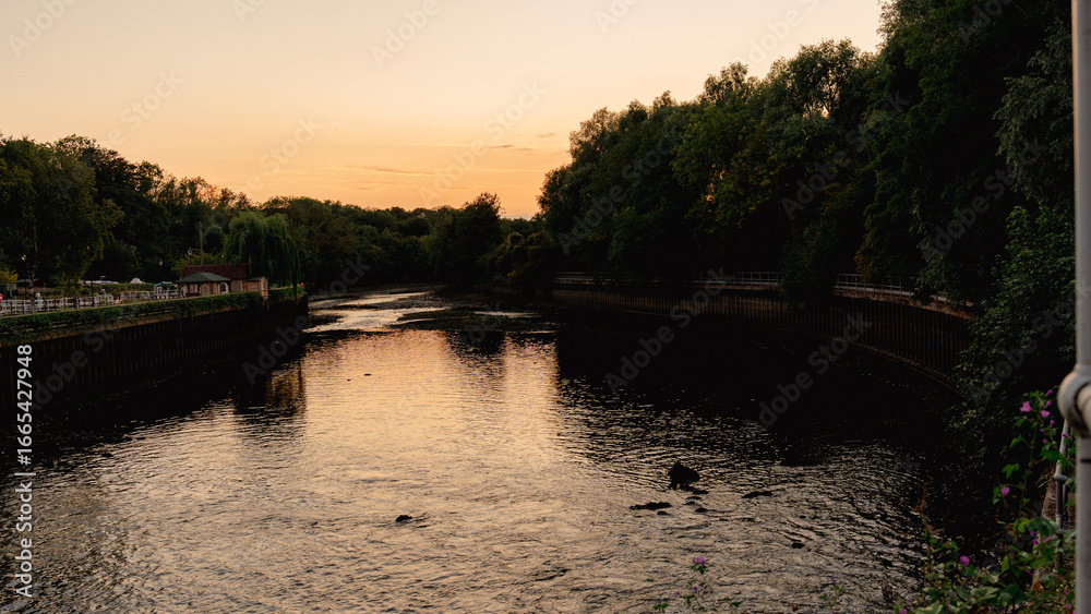 Fototapeta premium A breathtaking golden hour sunset with vibrant colors reflecting perfectly on the calm water near a historic lock and dam. This peaceful scene embodies tranquility and the beauty of nature's cycles.