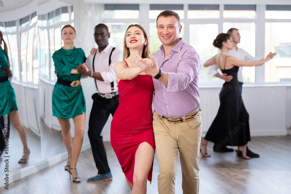 Naklejka premium Gracious man and young woman practicing waltz in pair in dancing studio