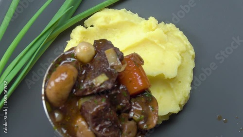 Appetizing pieces of meat bourguignon fall on mashed potatoes in a plate. Gravy with vegetables. Top view. High quality 4k footage