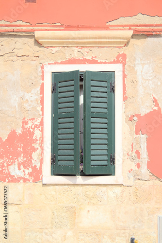 Rustic Venetian window with peeling wall and green shutters