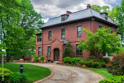 Tableau sur toile Elegant historic brick house with lush landscaped garden and winding driveway in