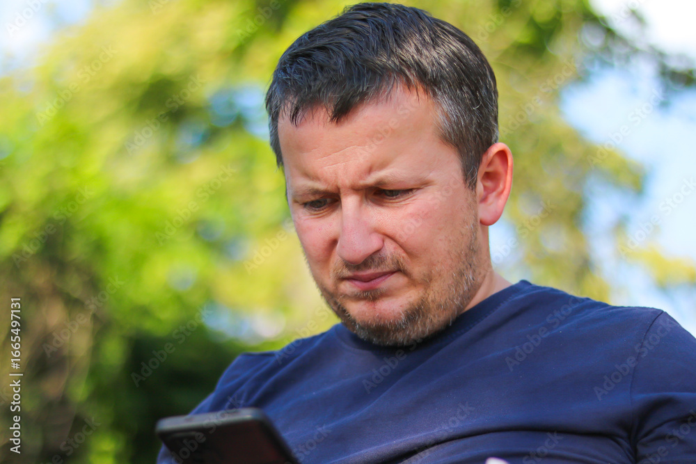 Man using smartphone outdoors with thoughtful expression Man using smartphone outdoors with thoughtful expression
