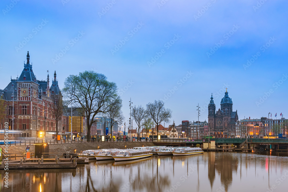 Fototapeta premium Amsterdam Netherlands, night city skyline at Amsterdam Central Station and Basilica of Saint Nicholas