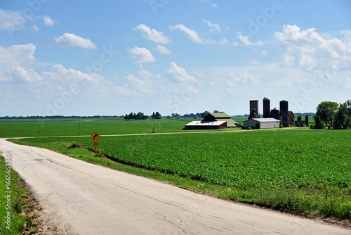 A country road winds around crop fields, barns and farms in northeastern Illinois forming a pastoral landscape.