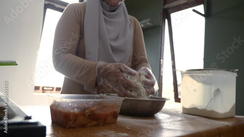 Asian muslim woman breading chicken, coatingmeat with flour before frying