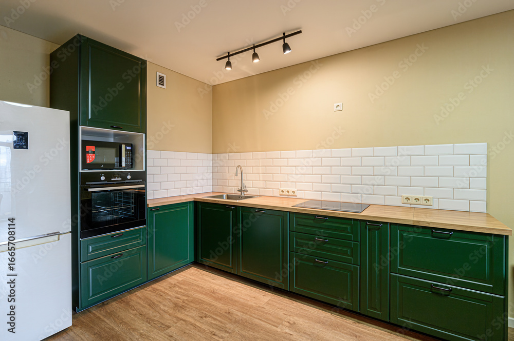 Fototapeta premium Modern kitchen with dark green cabinets, light wood countertops, white tiled backsplash, and stainless steel appliances
