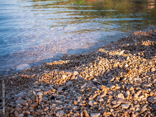 Fototapeta Naklejka Na Ścianę i Meble -  Pebble beach with small limestone stones and clear Adriatic Sea water, photographed in Croatia, showing typical Mediterranean coastal shoreline.
