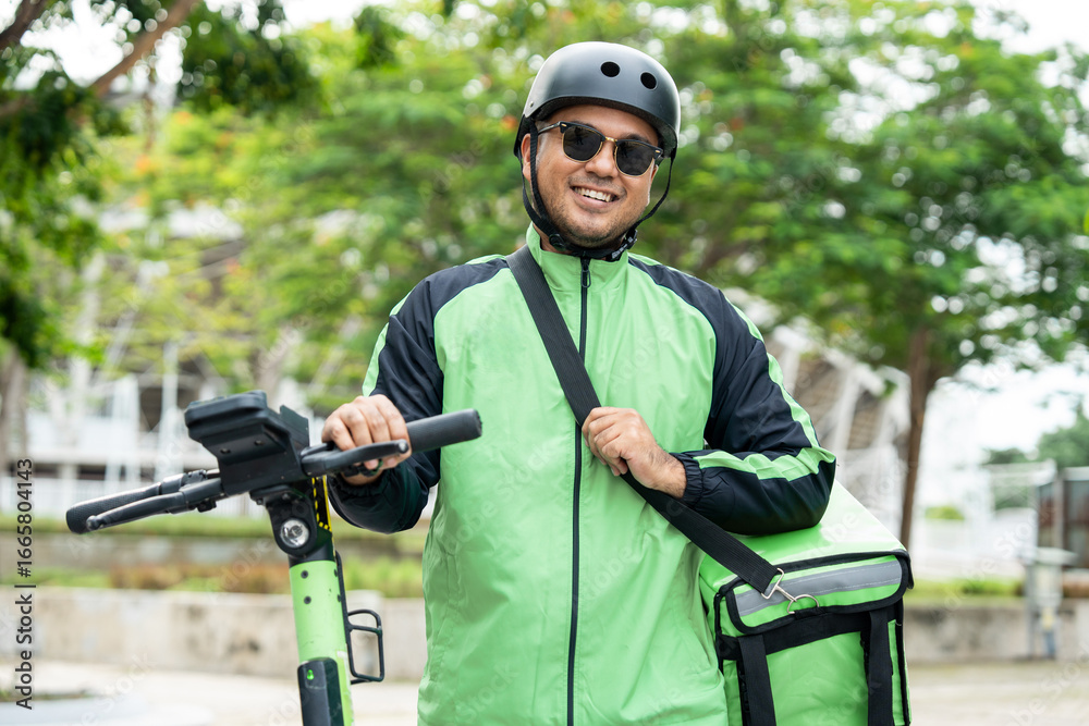 Obraz premium Rider food delivery man wearing green uniform and helmet ride the EV scooter delivery food service to customer. Happy delivery man with green backpack shipping of goods to customers by scooter