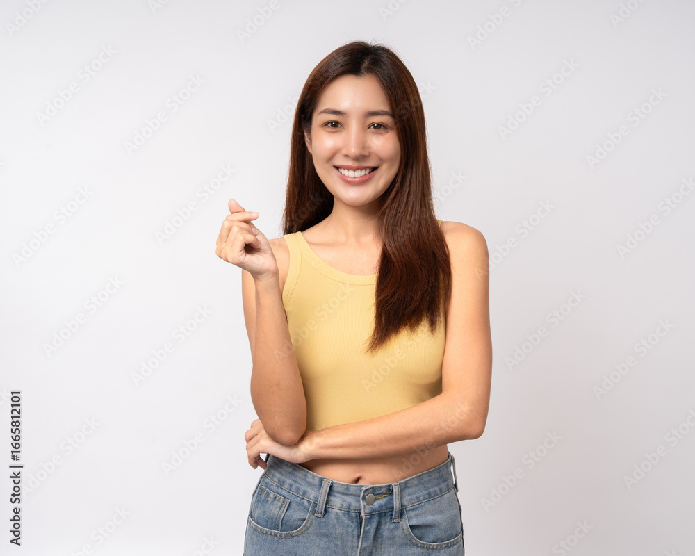 Pretty Young beautiful Asian woman standing and smiling showing mini heart sign on isolated white background. Lovely Latin female wearing yellow shirt feeling surprised and happy.