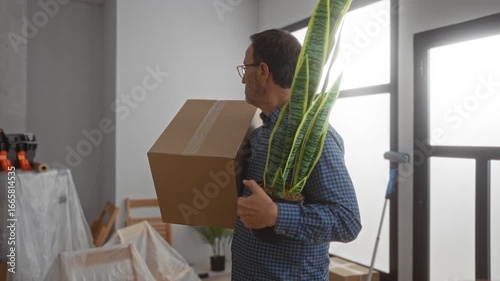 Man holding box and plant in new home interior surrounded by unpacked furniture and bright light