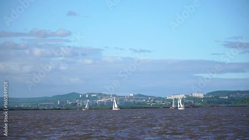 Sailboats are sailing on a lake. The sailboat is white . The sky is cloudy