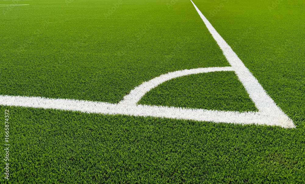 Fototapeta premium The football field corner with artificial green grass. Line in corner area of soccer field. Photo of a green synthetic grass sports field with white line shot from above. Football grass field corner.