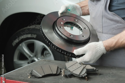 An auto mechanic prepares the replacement of the brake disc and brake pads. On the desktop, an auto mechanic inspects and controls spare parts-a new brake disc and a set of brake pads.