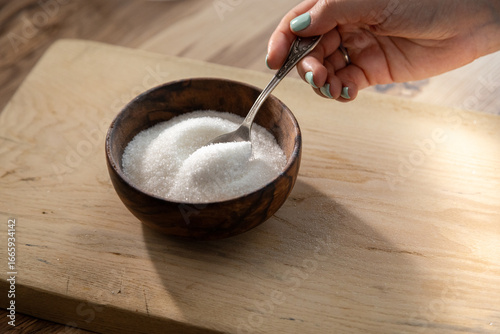 Canvas Print Granulated sugar filled in wooden bowl and hand with a spoon