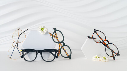 Three pairs of plastic eyeglass frames on white background with flowers. Eyewear fashion collection banner. Trendy eyeglasses still life minimal style. Optic store discount sale, promotion. Copy space