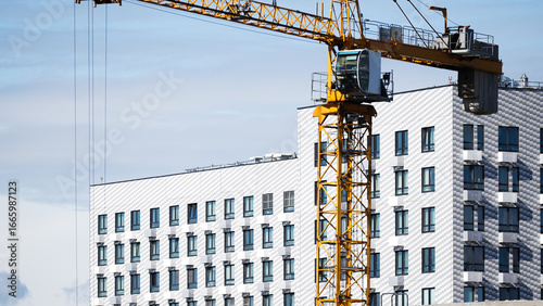 Yellow tower crane working on construction site near a modern high-rise residential building with many windows, urban development concept 
