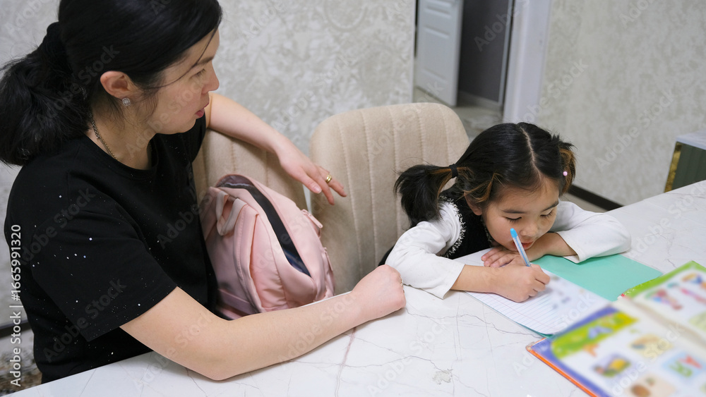 Obraz premium A woman helps a little girl write. The tutor is sitting with the child. Education and training. My daughter is doing her homework