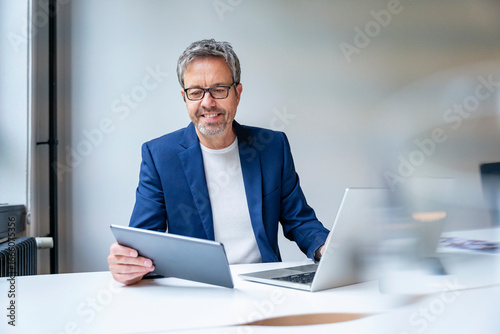Confident businessman working with tablet and laptop at office desk