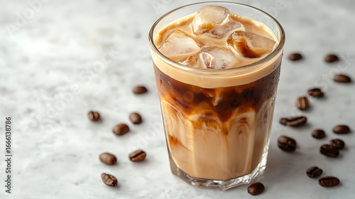 Glass of iced coffee with milk and ice cubes on light surface, surrounded by scattered coffee beans, creating refreshing and inviting beverage scene