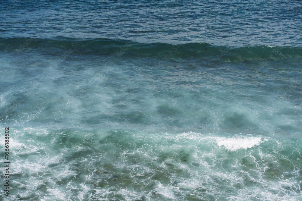 Fototapeta premium Blue ocean waves with white foam rolling on the surface of clear water.
